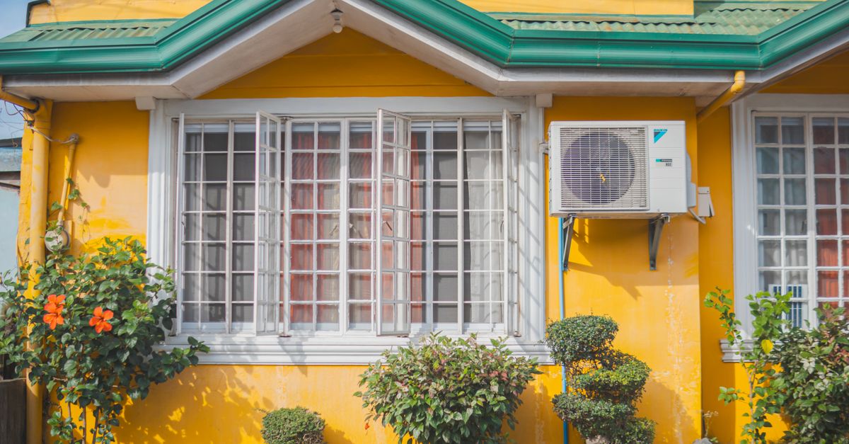 Unité extérieure de climatisation fixée sur la façade d'une maison avec jardin